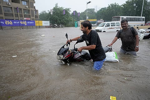 Men push their motorcycle through a flooded road in Ahmedabad